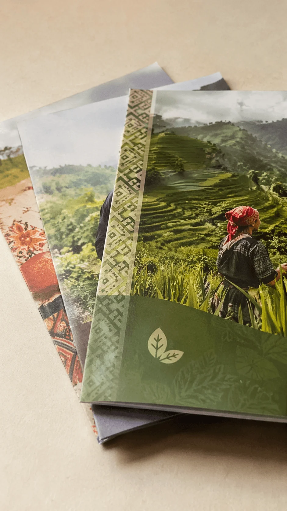 Stacked brochures featuring cultural and sustainability themes with a person in traditional attire in a lush terraced landscape and decorative patterns on the covers