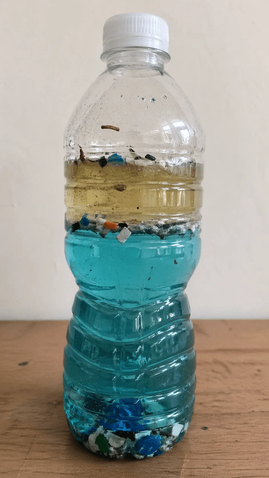 Plastic bottle showing layers of polluted water with oil and floating debris illustrating ocean pollution