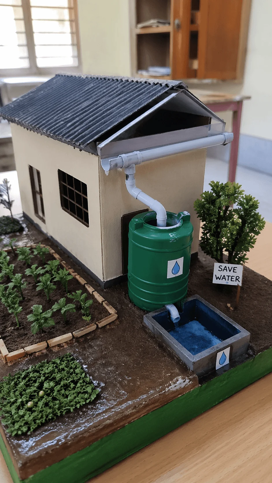 Model of a house with a rainwater harvesting system collecting roof water into a storage tank and reuse basin with garden and save water sign