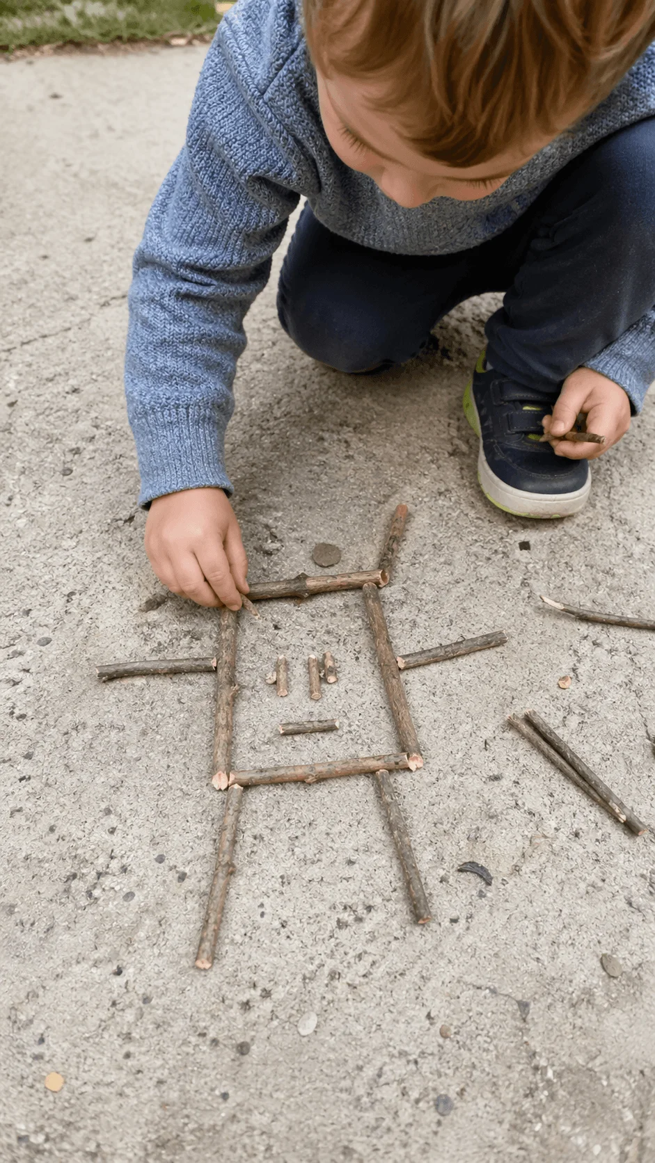 Toddler arranging sticks and twigs on the ground to create a simple shape or pattern outdoors
