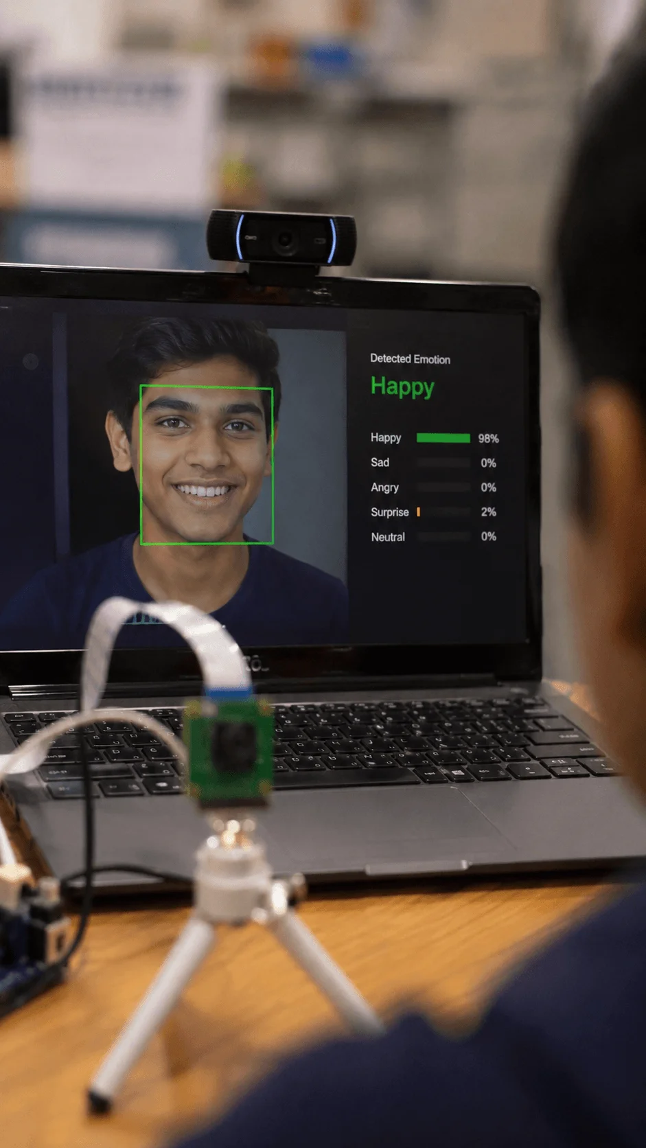 AI emotion detection camera project showing a person smiling on a laptop screen with facial recognition software identifying happy emotion and displaying emotion percentage analysis in real time