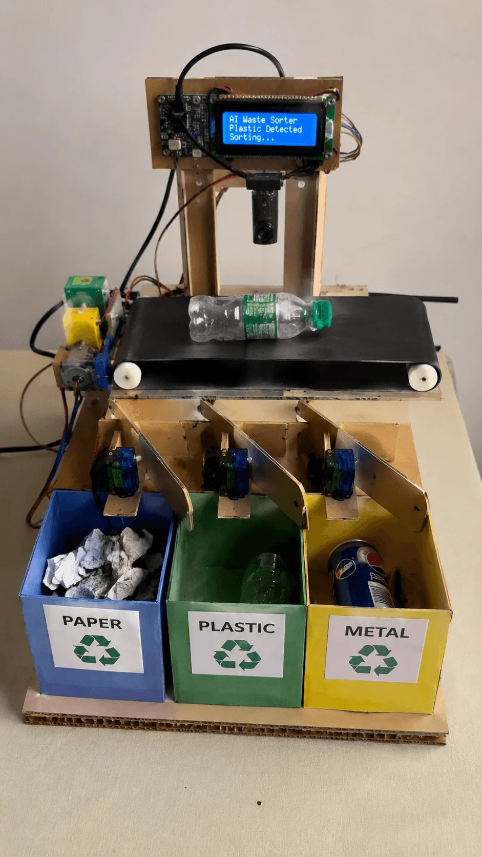 AI powered waste sorting machine project with conveyor belt system detecting a plastic bottle and sorting waste into paper plastic and metal bins using sensors and a digital display screen