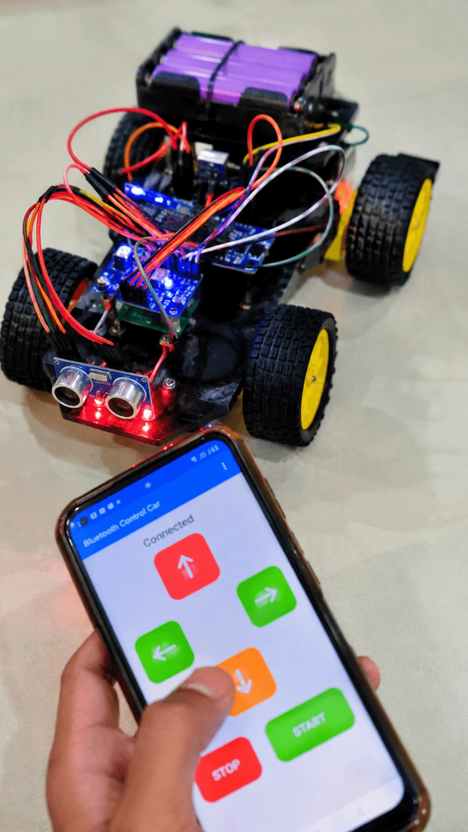 Bluetooth controlled robot car with ultrasonic sensors and electronic components operated through a smartphone app showing directional controls and start stop buttons