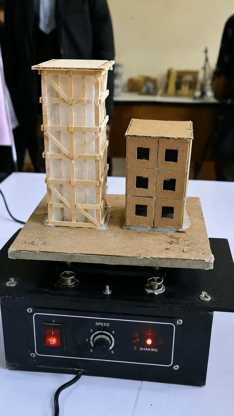 Earthquake resistant building model project with miniature cardboard buildings placed on a shaking platform machine demonstrating structural stability and vibration testing during simulated earthquake conditions