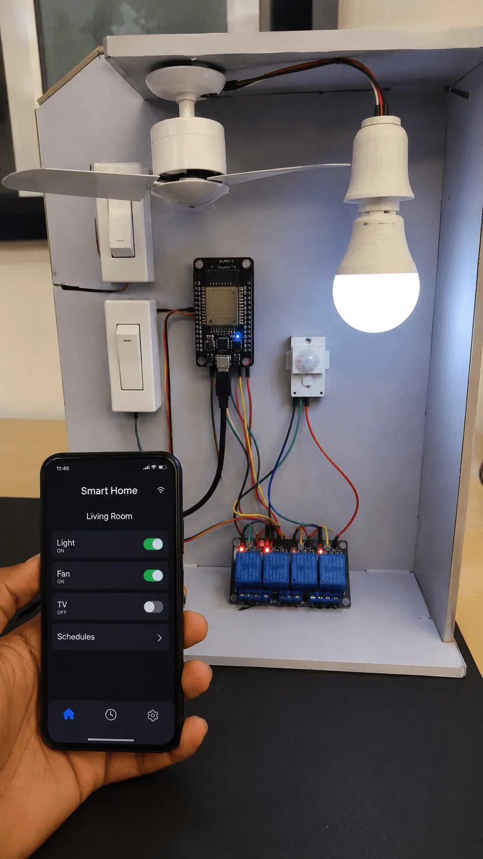 Smart home automation project with mobile app controlled light bulb and ceiling fan using sensors relays and microcontroller setup displayed inside a model smart room system