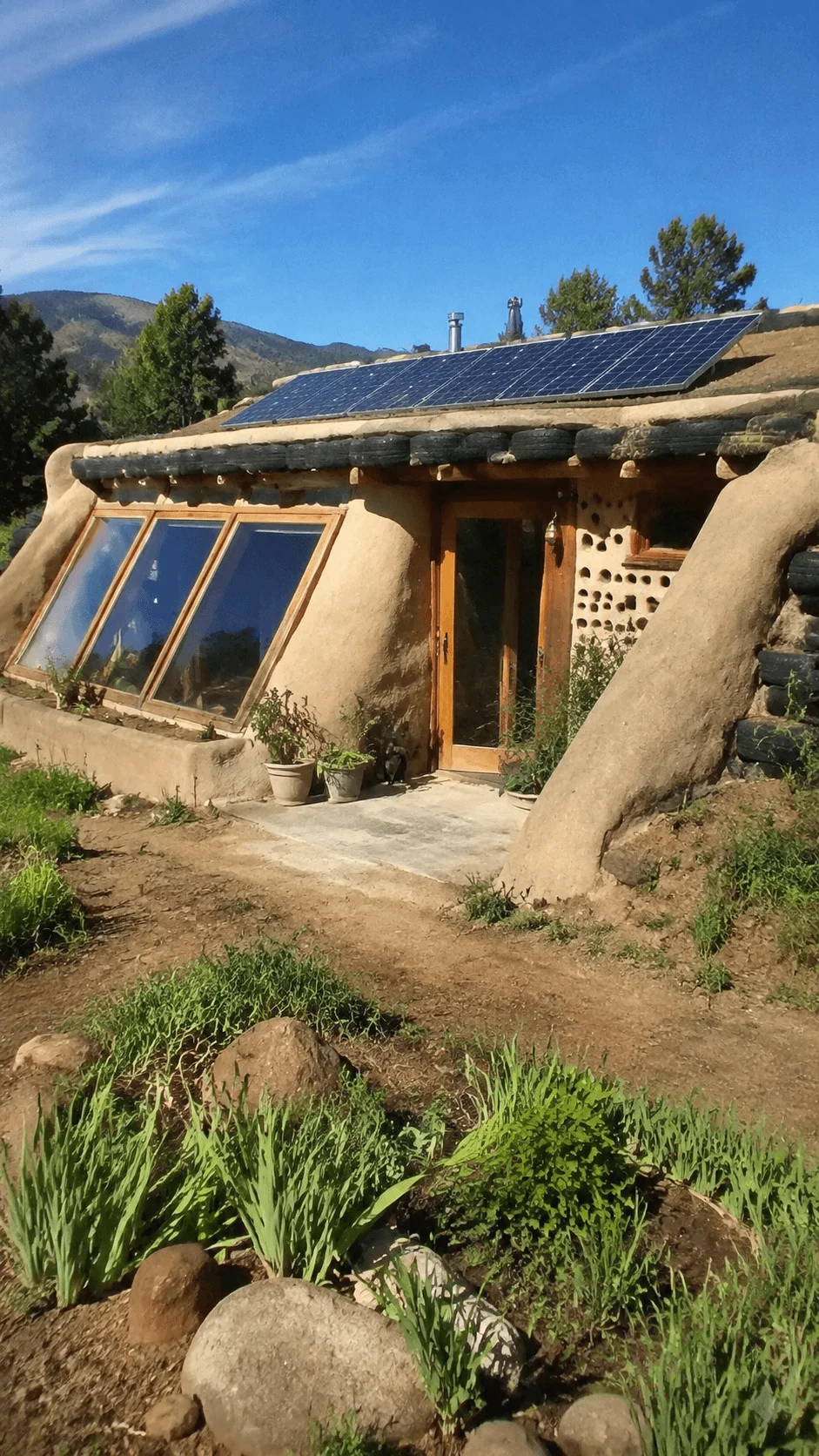 Earthship inspired natural building eco friendly home with solar panels earth walls large windows and sustainable architecture surrounded by a green landscape