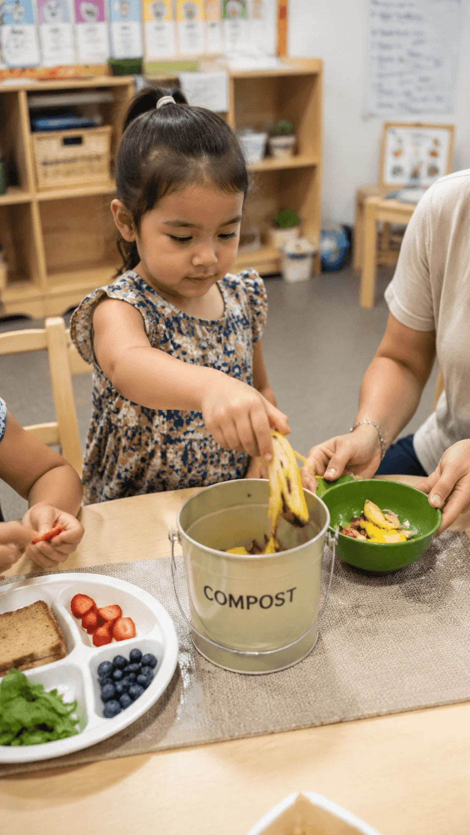 Children learning about food waste reduction by placing fruit scraps into a compost container during a preschool sustainability activity
