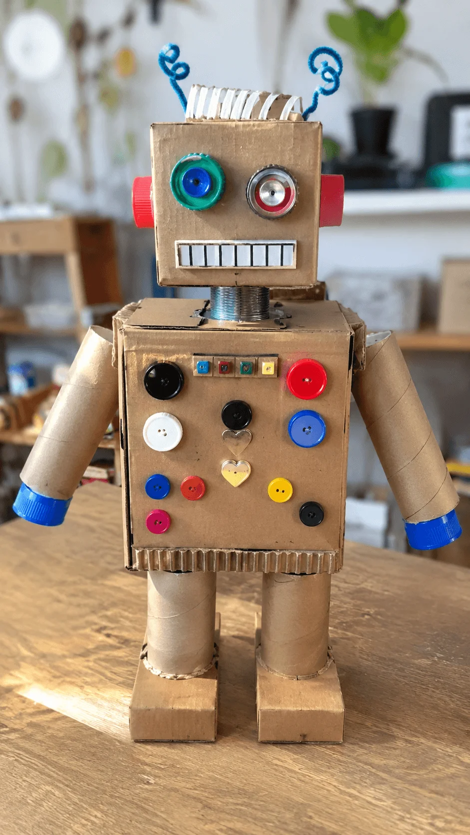 Junk robot craft made from recycled cardboard tubes boxes bottle caps buttons and wire featuring a colorful handmade robot standing on a table as a creative upcycling art project for kids.