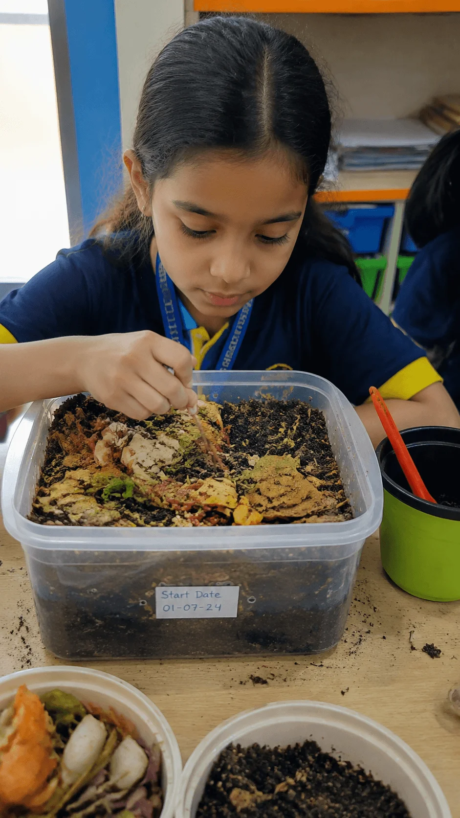 Student conducting a mini compost science experiment by observing organic waste decomposition in a classroom compost container