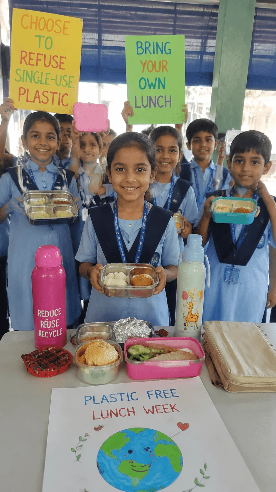 Students participating in a plastic free lunch week activity with reusable lunch boxes bottles and environmental awareness posters at school