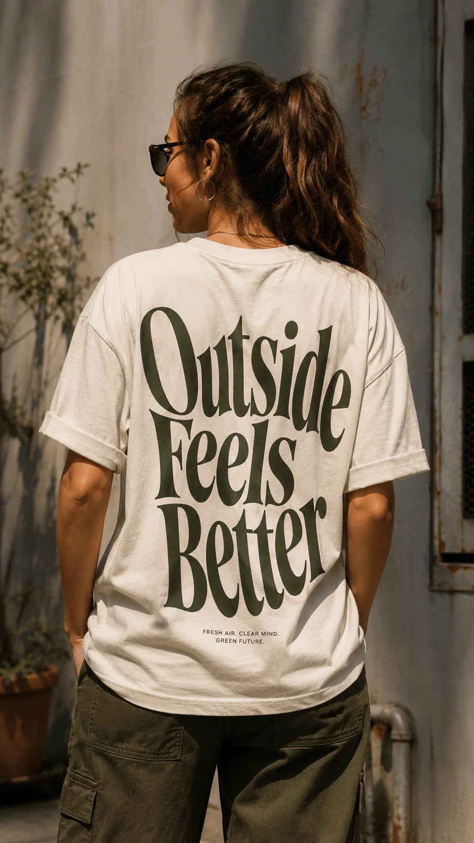 Sustainable typography T shirt featuring oversized green lettering with the phrase Outside Feels Better worn outdoors
