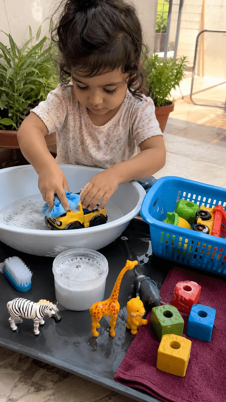 Toddler washing a toy truck with a reusable sponge at an outdoor toy cleaning station