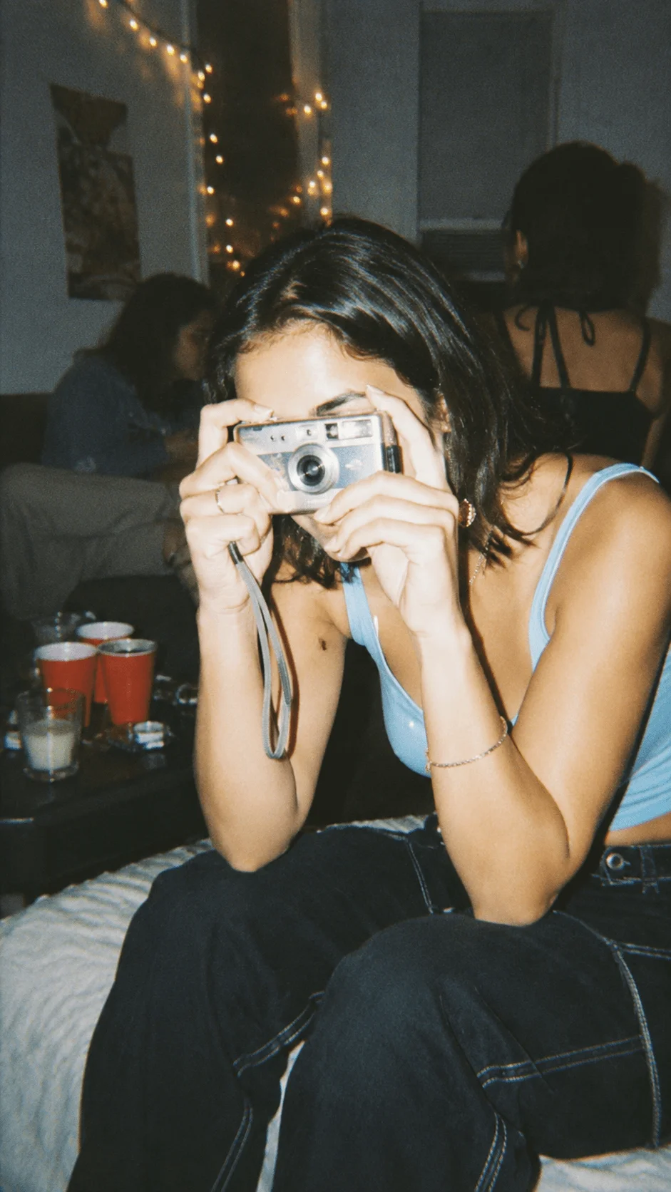 90s and Y2K film camera aesthetic with a person taking a vintage photograph at a casual indoor gathering