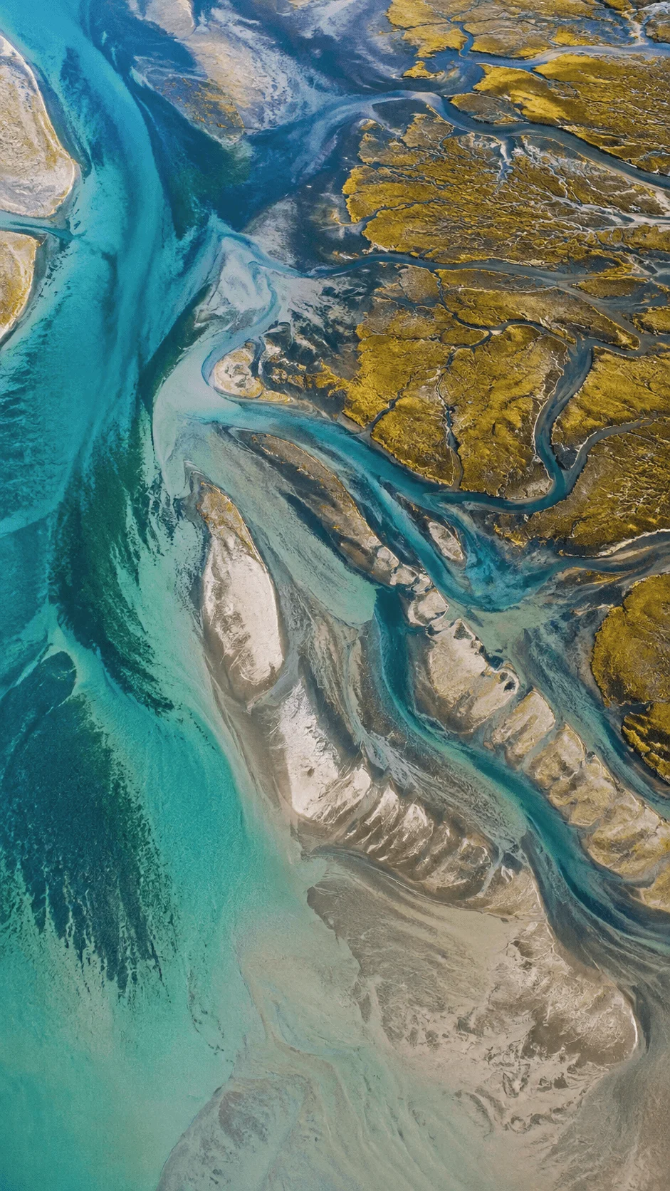 Aerial view of intricate turquoise waterways winding through sandy river islands and golden brown vegetation, creating an abstract natural pattern.