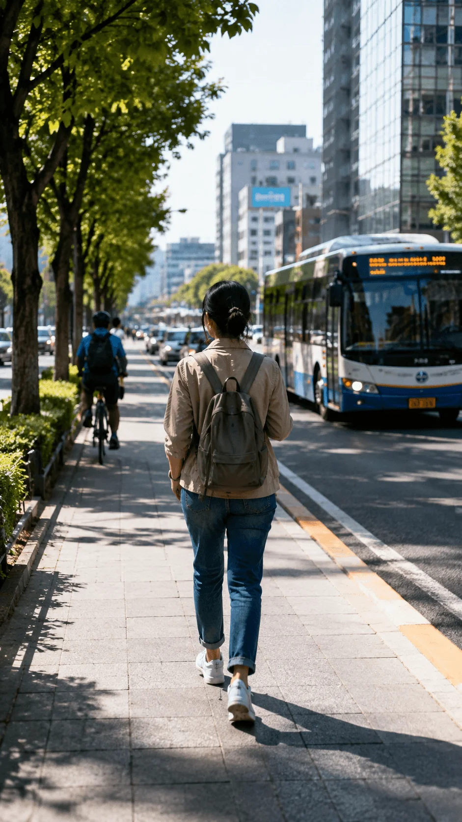 Woman walking along a city sidewalk beside a cyclist and public bus representing sustainable transportation choices