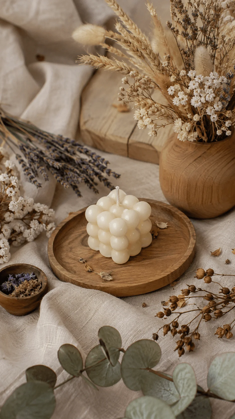 Dried botanical materials with preserved flowers eucalyptus leaves wheat stems candle and wooden accessories arranged in a natural sustainable photography composition