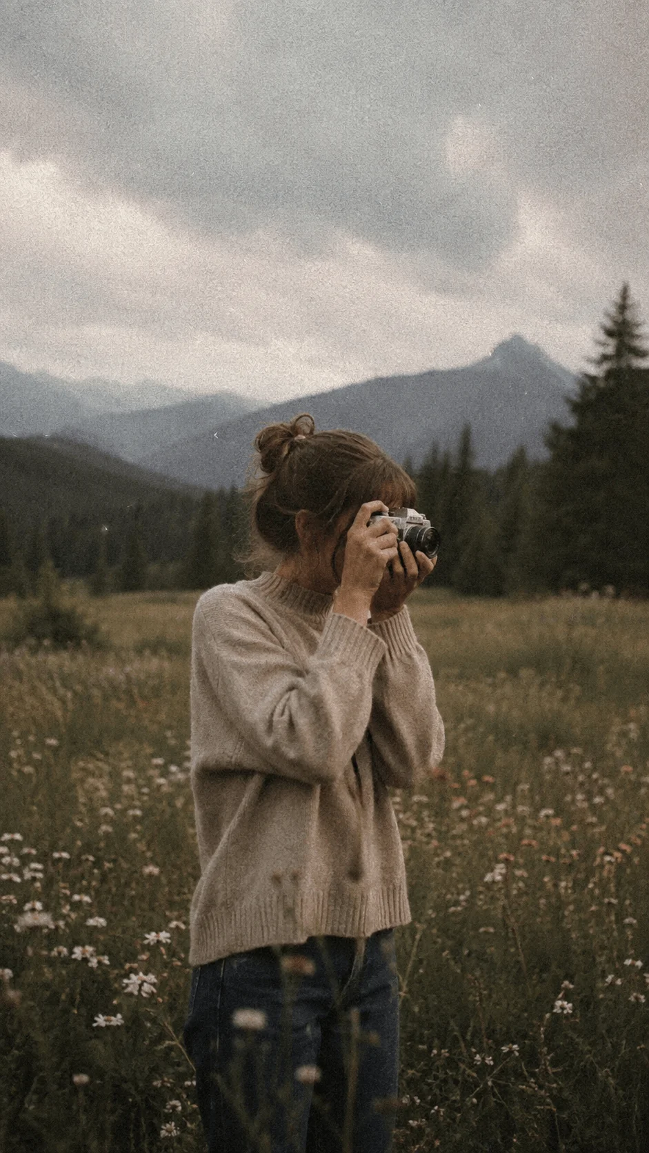 Film photographer capturing a mountain landscape in a wildflower meadow with natural film grain and a vintage aesthetic