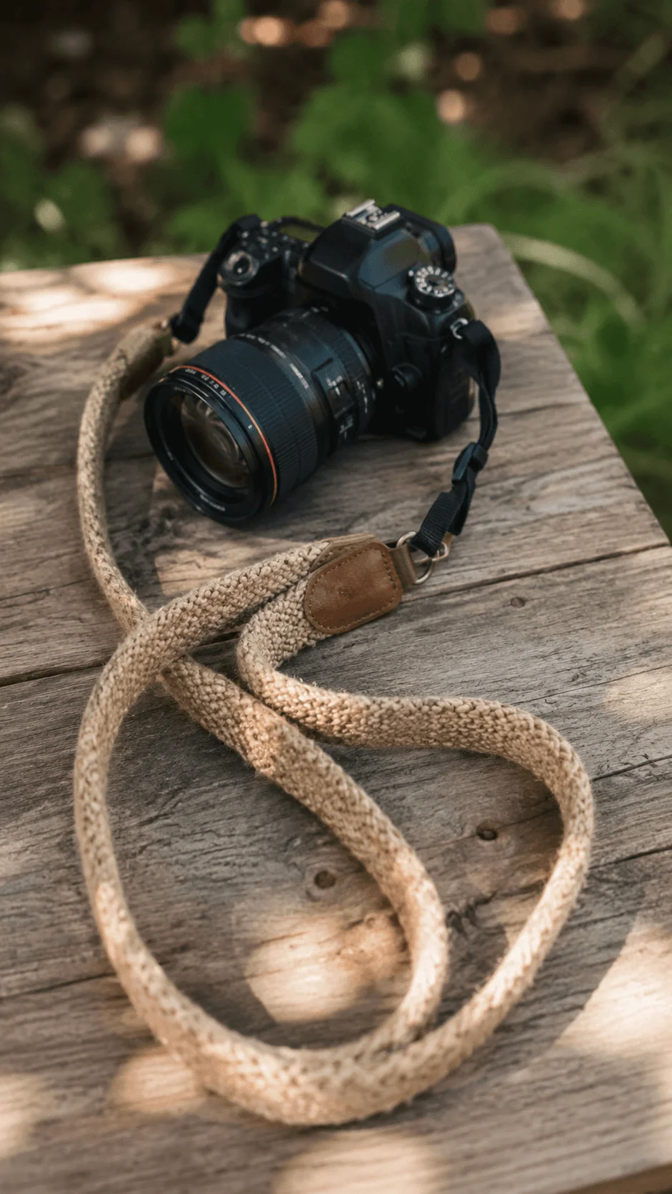 Hemp and recycled camera strap attached to a camera resting on a rustic wooden table in a natural outdoor setting.