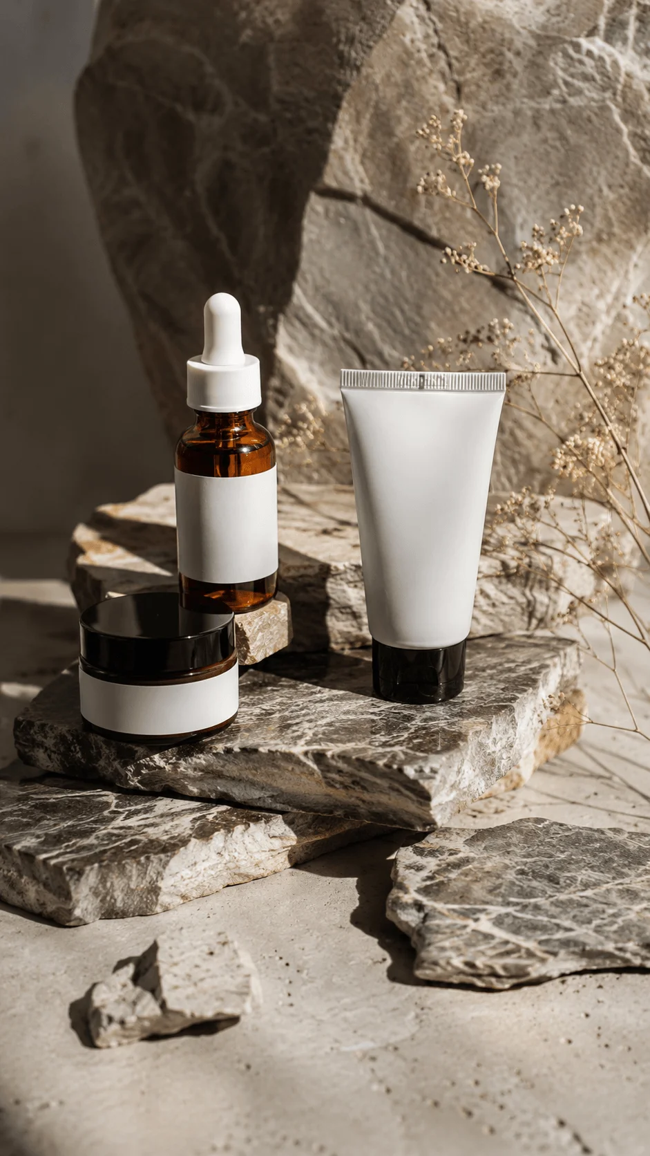 Natural stone photography props featuring skincare containers on textured stone slabs with dried flowers and warm natural lighting