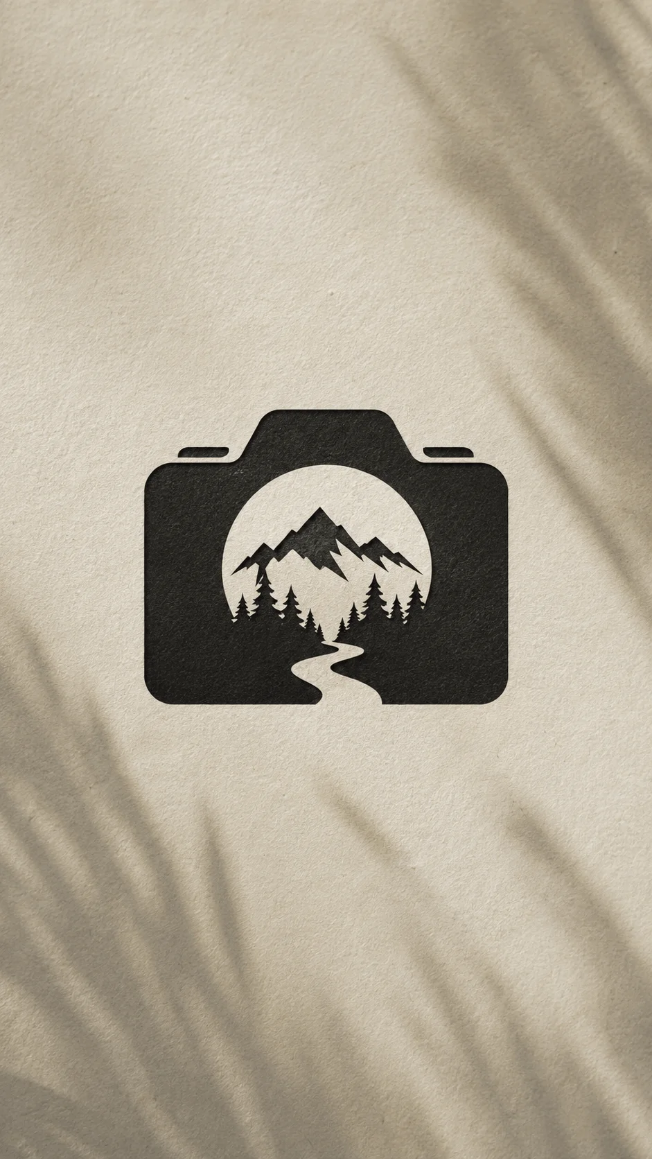 Negative space nature logo featuring a camera silhouette with mountains, pine trees, and a winding path inside on a textured neutral background