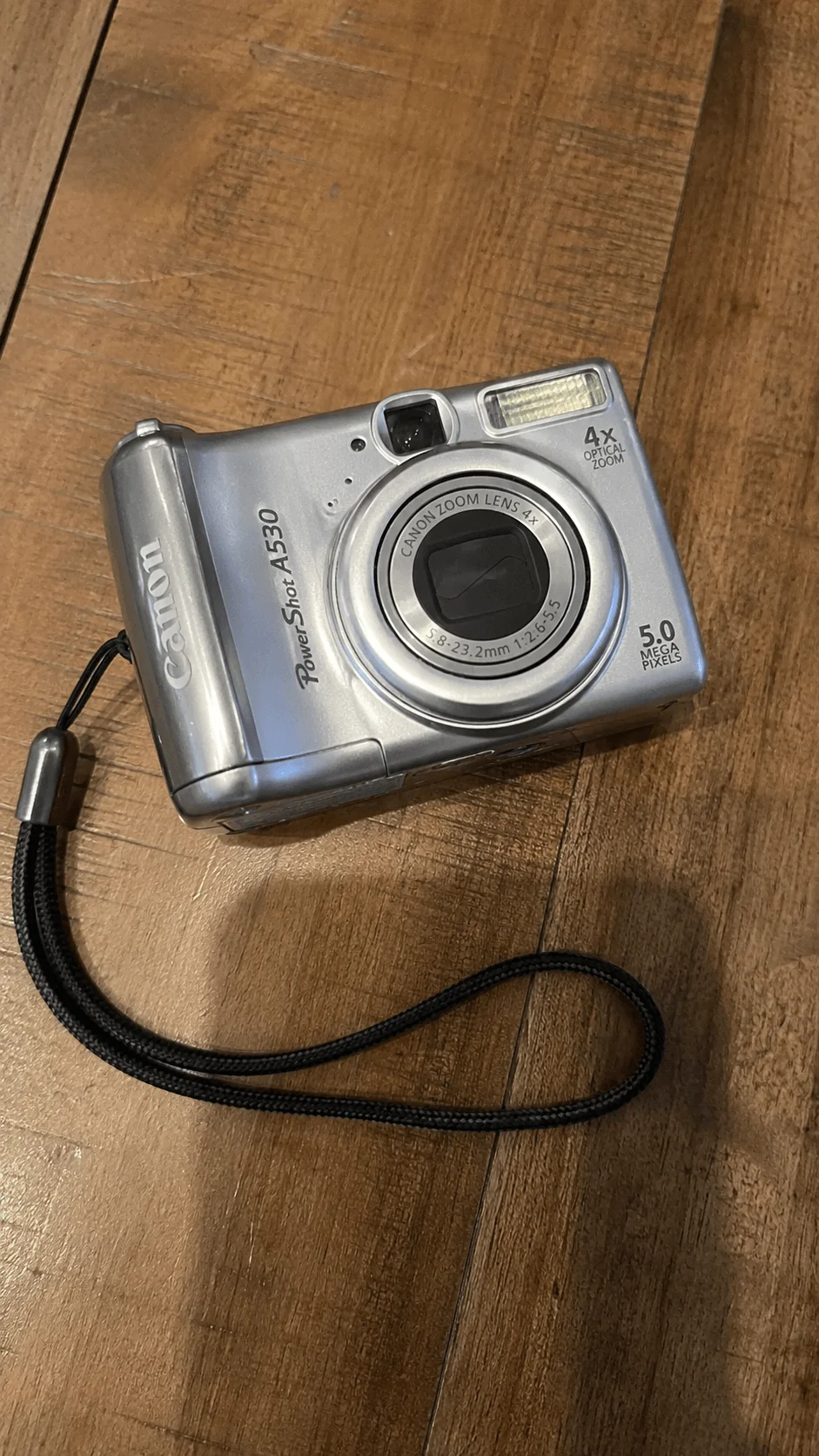 Vintage silver digital camera with a 4x optical zoom lens and wrist strap on a wooden surface