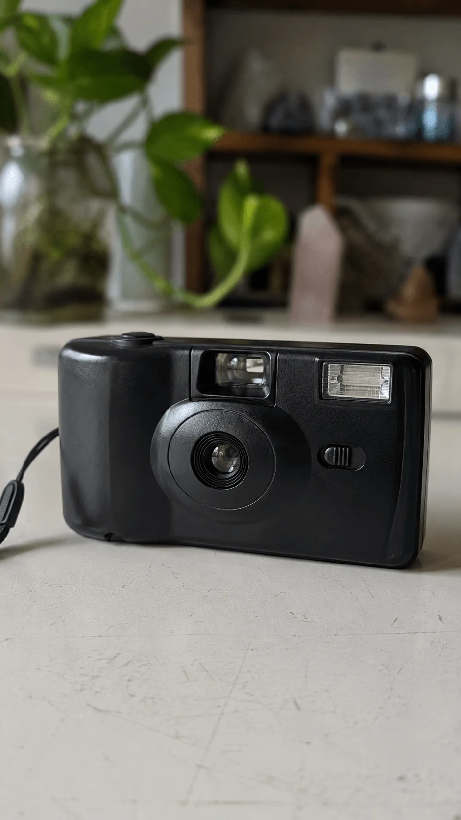 Reusable 35mm film camera on a table with green plants in the background and a vintage minimalist setting