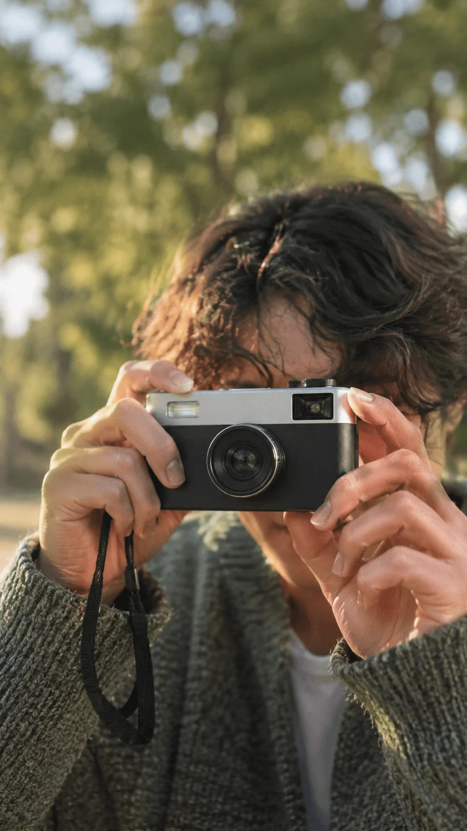 Person using a compact camera outdoors surrounded by trees and natural light