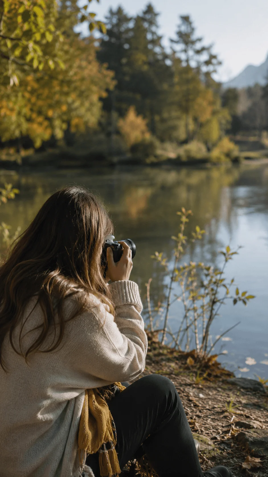 Woman practicing slow photography beside a peaceful lake surrounded by autumn trees and mountains using a camera in natural light