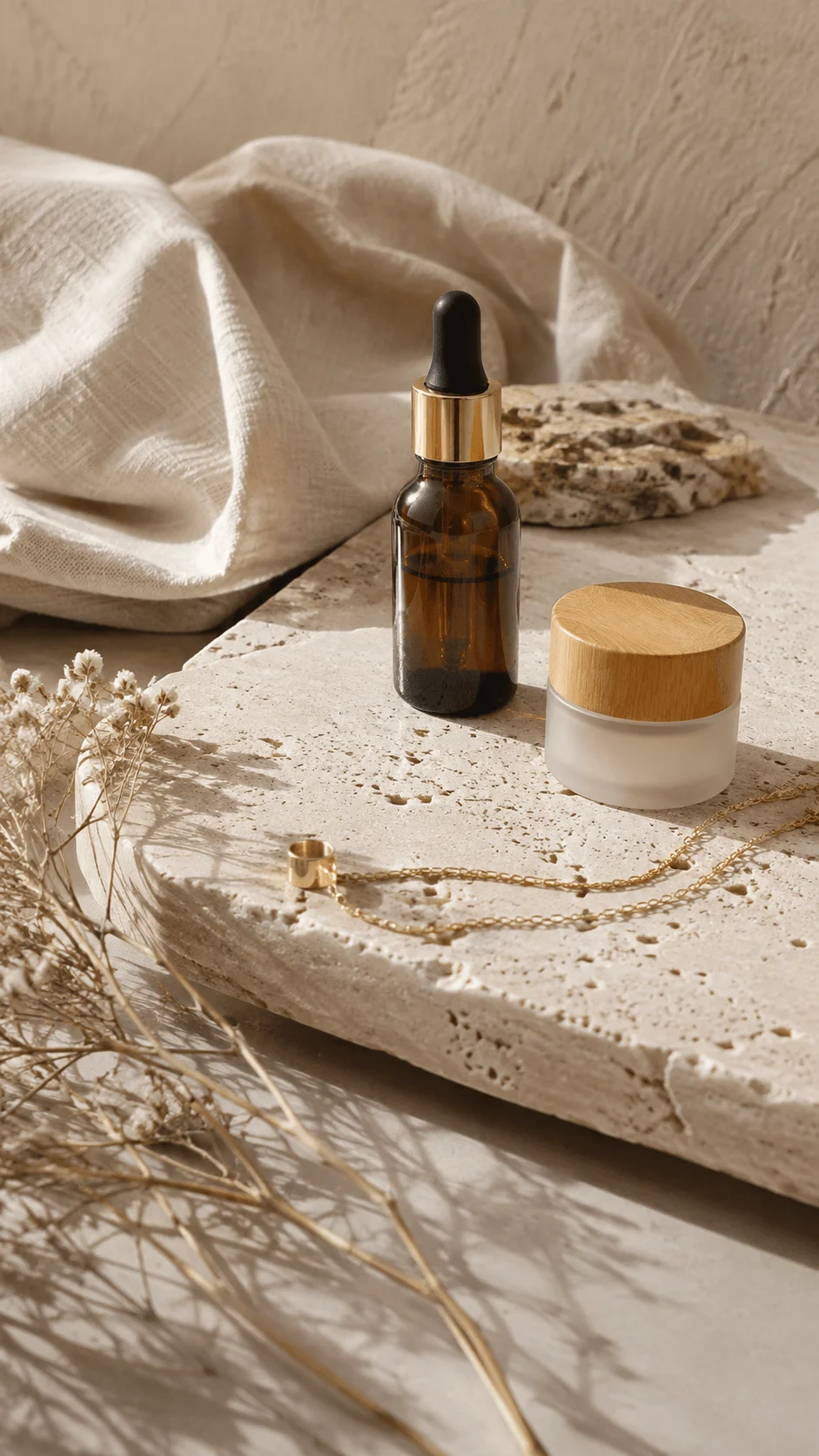 Stone and travertine surface with skincare bottle ceramic container gold jewelry and dried flowers arranged in a luxury sustainable photography setting