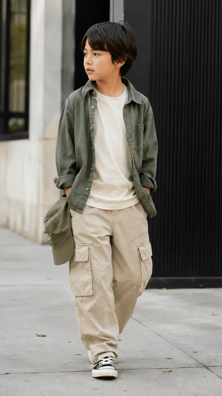 Young boy wearing a green overshirt white shirt and beige cargo pants with sneakers outdoors