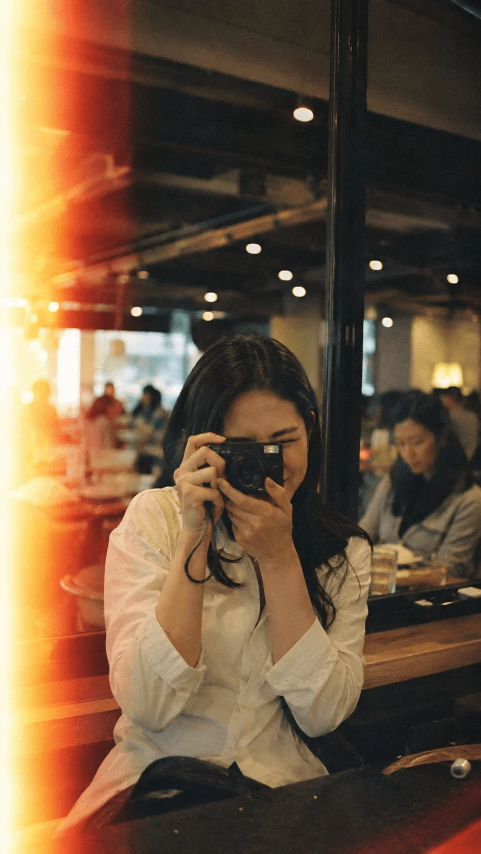 Person taking a film photograph in a cafe with warm lighting, light leaks and an imperfect vintage film aesthetic