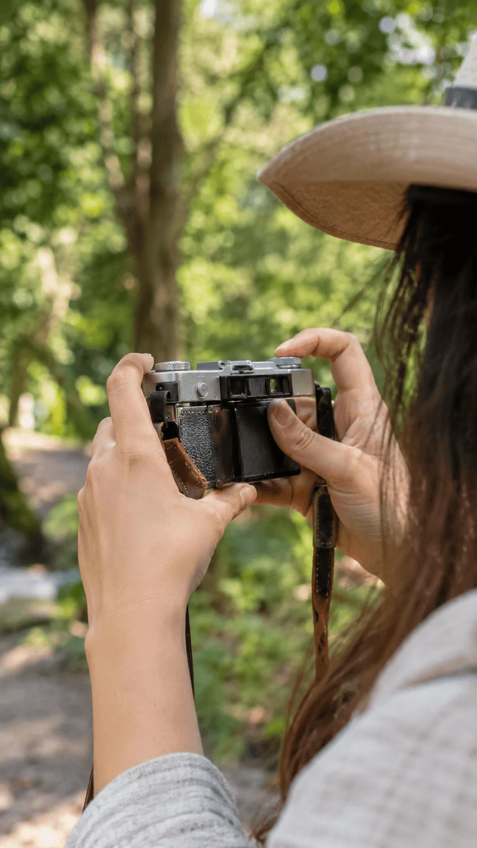 Person using a vintage film camera outdoors in a lush green forest with a natural screen free photography approach