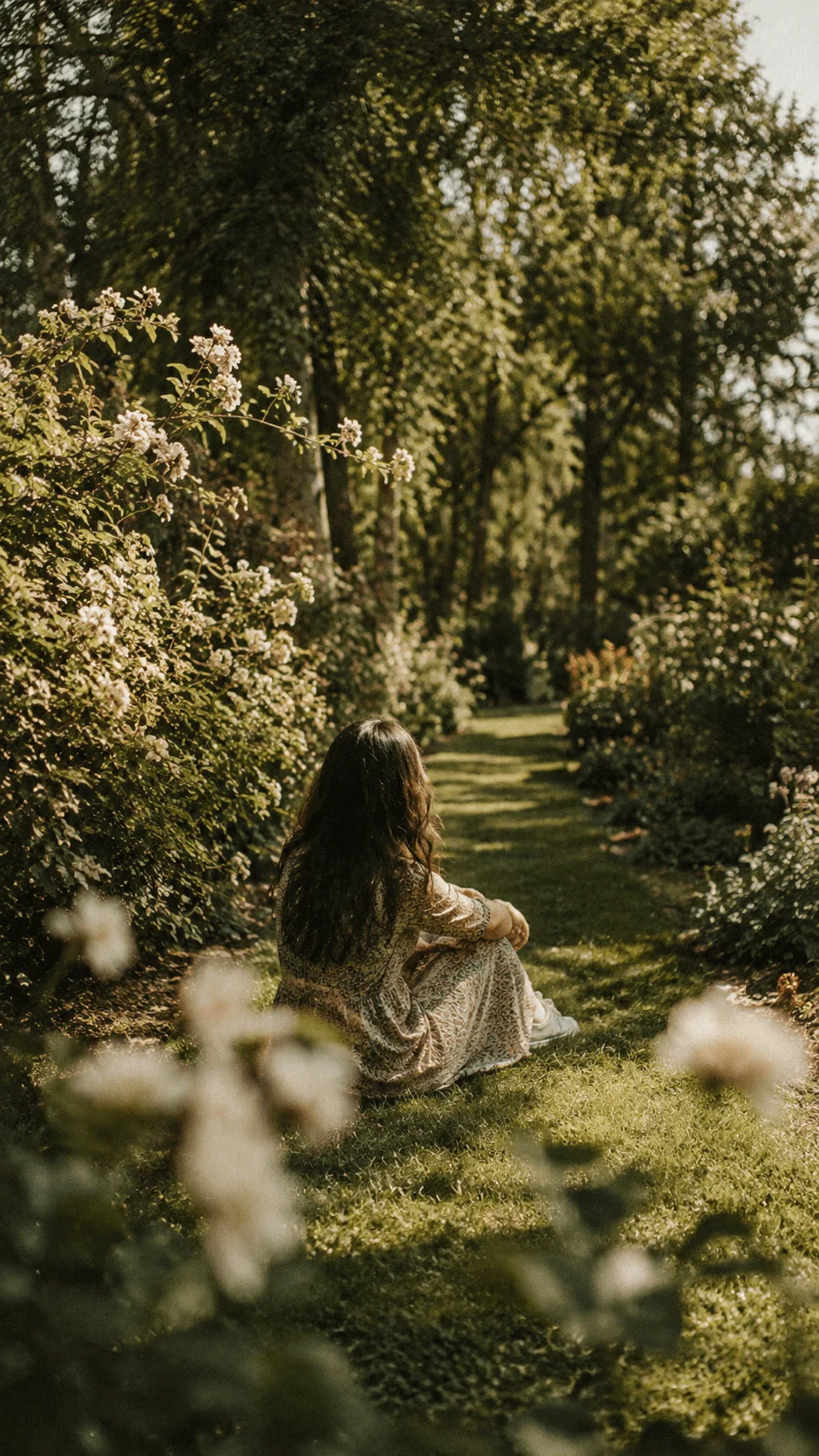 Vintage Film Inspired Nature Photography featuring a woman sitting in a lush garden surrounded by trees, flowers and soft warm sunlight with a nostalgic natural atmosphere