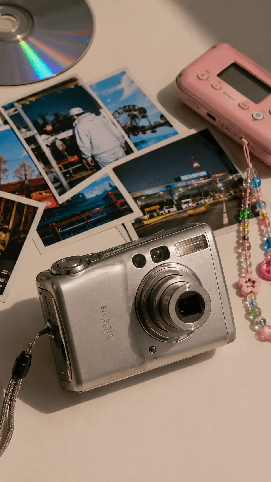 Y2K digital cameras and printed photographs arranged with a pink camera, colorful beaded strap, and compact silver camera