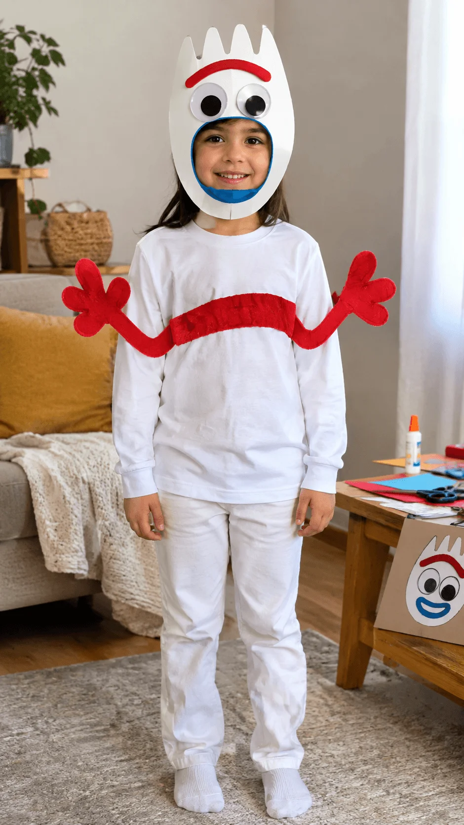 Recycled Forky Halloween costume for kids made with a white outfit, a handmade cardboard mask with googly eyes and colorful facial details, and red pipe cleaner arms, showing a creative DIY costume idea using recycled craft materials indoors